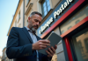 Homme d'affaires inquiet lisant des nouvelles financières sur sa tablette devant une agence Banque Postale